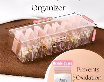 May include: Clear plastic jewelry organizer with pink dividers. The organizer is labeled "Anti Tarnish Jewelry Organizer" and measures 10.43 inches long, 3.94 inches wide, and 2.95 inches high. A small bag is shown with the text "Usable Space" and "Prevents Oxidation".