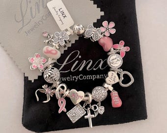 Op de afbeelding: Een zilveren armband met roze en witte bedels, waaronder een hartbedel met de tekst "Ik hou van je", een bedel met de tekst "Hoop" en een bedel met de tekst "Linx Jewelry Company".