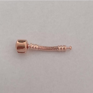 May include: A rose gold charm bracelet with a curved, snake-like chain. The charm is a small, round, rose gold bead.