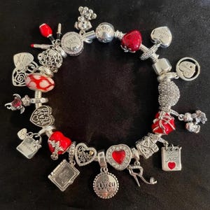 Puede incluir: Un brazalete de plata con dijes rojos y blancos. Los dijes incluyen corazones, una caja de regalo, un l&aacute;piz labial, una rosa y un dije que dice "Wifey".