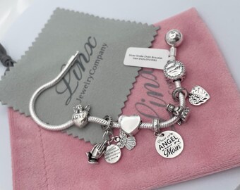 May include: Silver charm bracelet with various charms, including a heart, angel wings, a praying hands charm, and a charm that says "Those on Angel wings are near Mom".