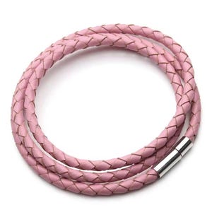 Puede incluir: Una pulsera envolvente de cuero trenzado rosa claro con un cierre magnético plateado. La pulsera está hecha de dos hebras de cuero trenzado y está diseñada para envolverse alrededor de la muñeca varias veces. La pulsera se muestra sobre un fondo blanco.