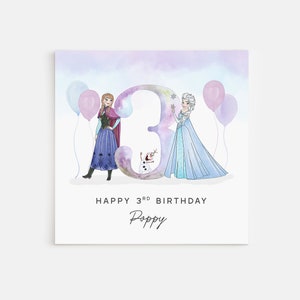 Puede incluir: Una tarjeta de cumplea&ntilde;os con una ilustraci&oacute;n de acuarela de Elsa y Anna de Frozen, de pie frente a un gran n&uacute;mero 3. La tarjeta tiene un fondo azul claro con globos rosas y morados. El texto "Happy 3rd Birthday Poppy" est&aacute; impreso debajo de la ilustraci&oacute;n.