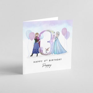 Puede incluir: Una tarjeta de cumplea&ntilde;os con una ilustraci&oacute;n de acuarela de Elsa y Anna de Frozen, de pie frente a un gran n&uacute;mero "3" con globos. La tarjeta dice "Feliz 3er cumplea&ntilde;os Poppy".