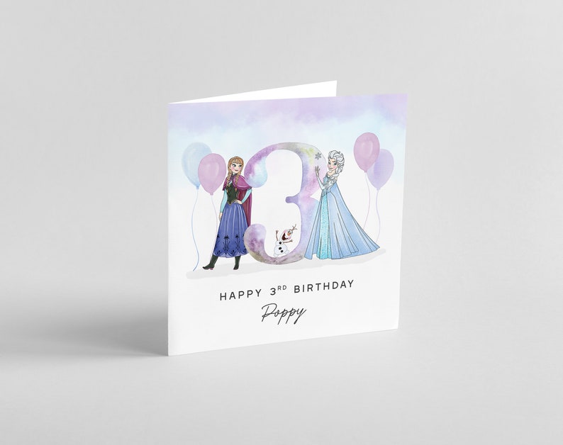 Puede incluir: Una tarjeta de cumplea&ntilde;os con una ilustraci&oacute;n de acuarela de Elsa y Anna de Frozen, de pie frente a un gran n&uacute;mero "3" con globos. La tarjeta dice "Feliz 3er cumplea&ntilde;os Poppy".