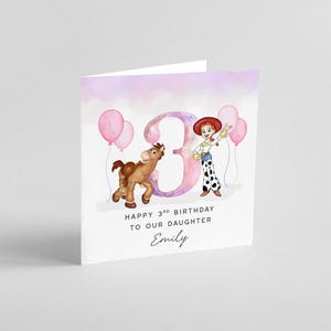 May include: A pink and purple watercolor birthday card with a cartoon image of a girl dressed as a cowgirl holding a pink balloon. The card says "Happy 3rd Birthday to our daughter Emily".