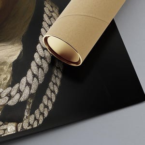 May include: A rolled brown cardboard mailing tube resting on a printed poster. The poster features a close-up of a person wearing multiple thick, silver-toned, diamond-encrusted cuban link chains over a dark jacket and a textured white neck scarf.