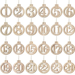 May include: A collection of twenty-four wooden Christmas ornaments, each featuring a different number from 1 to 24. The ornaments are circular with a cutout number and a string for hanging. The wood has a natural, light brown color.
