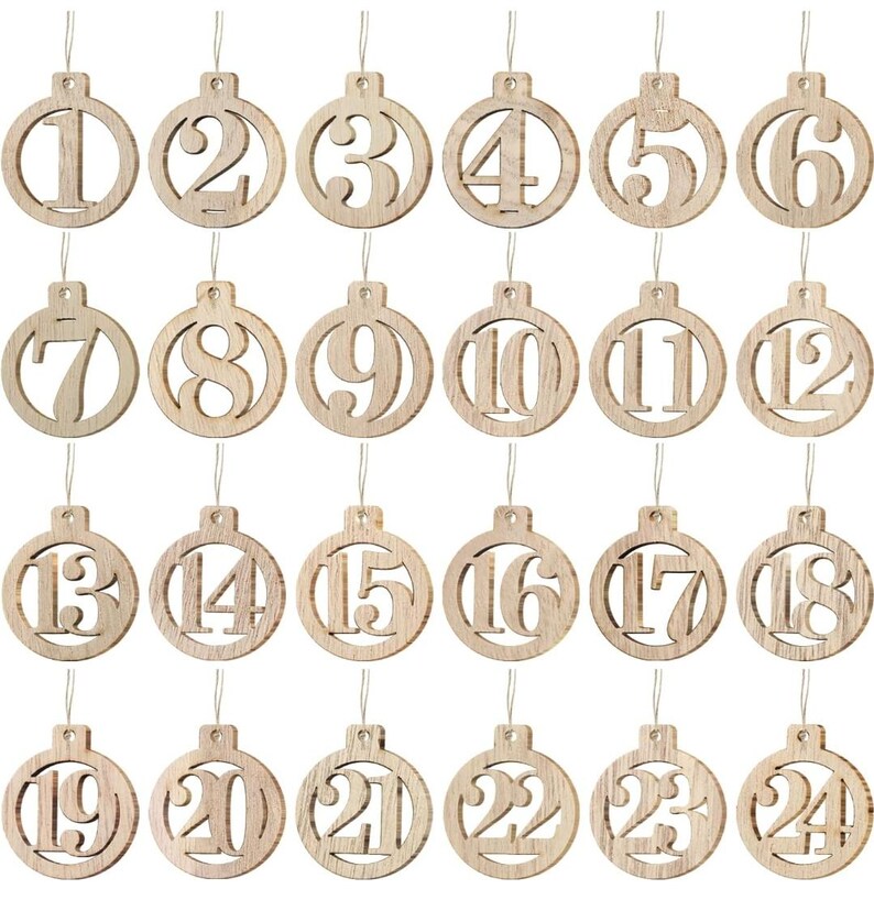 May include: A collection of twenty-four wooden Christmas ornaments, each featuring a different number from 1 to 24. The ornaments are circular with a cutout number and a string for hanging. The wood has a natural, light brown color.