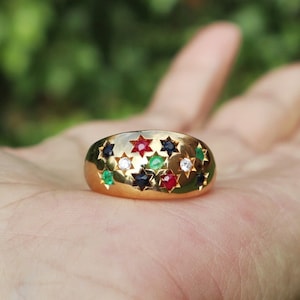 May include: A gold ring with a raised design of stars set with red, green, black, and white gemstones.