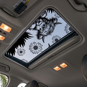 Puede incluir: Techo solar de coche con un diseño floral en blanco y negro y una silueta de bisonte. El diseño incluye girasoles y una cabeza de bisonte. El interior del coche es visible.