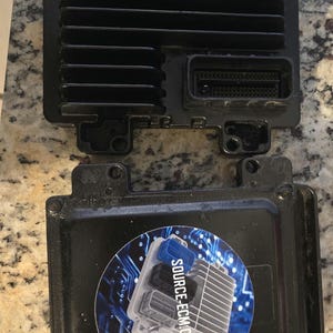 May include: A black automotive engine control module (ECM) with multiple connectors and a sticker that says "SOURCE-ECM.COM".