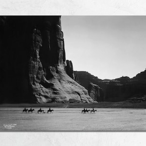 May include: Black and white photograph of a group of people on horseback riding through a desert canyon. The people are silhouetted against the bright sky, and the canyon walls are tall and imposing.