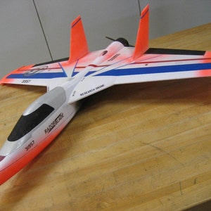 Könnte beinhalten: Ein weißes, orangefarbenes und blaues Modellflugzeug mit den Worten "Razorblade" und "Research Drone" auf der Seite. Das Modellflugzeug hat ein schwarzes Cockpit und einen Propeller.