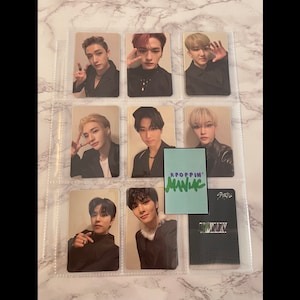 May include: A set of eight photo cards featuring a K-pop boy band. The cards are in a clear plastic sleeve. The cards are black and white with a slight sepia tone. The cards feature the band members in various poses. The cards are labeled with the band's name, "Stray Kids", and the album title, "ODDINARY".