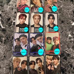 May include: A collection of twelve trading cards featuring images of various individuals. Each card has a unique design and includes text such as names, dates, and the word "ODD". The cards are arranged on a textured surface.