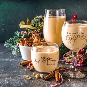 May include: Two glasses of eggnog with festive Christmas decorations. One glass says "Just here for the eggnog" and the other says "Let's get lit".