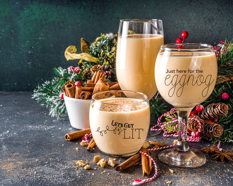 May include: Two glasses of eggnog with festive Christmas decorations. One glass says "Just here for the eggnog" and the other says "Let's get lit".