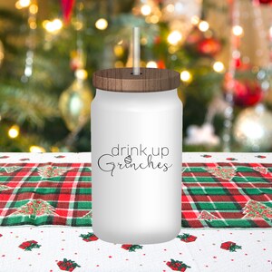 May include: White tumbler with a wood lid and a straw. The tumbler has the text "drink up Grinches" with a small Christmas tree ornament graphic.