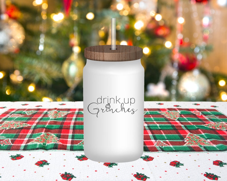 May include: White tumbler with a wood lid and a straw. The tumbler has the text "drink up Grinches" with a small Christmas tree ornament graphic.
