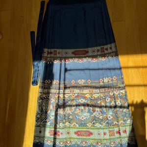 May include: A navy blue pleated skirt with a decorative patterned border. The border features red, yellow, and blue floral and paisley designs. The skirt has a matching navy blue tie.