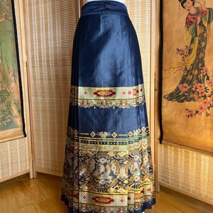 May include: A navy blue skirt with a decorative gold and red patterned border. The skirt is pleated and has a high waist. The lower border features a detailed design with birds and floral motifs.