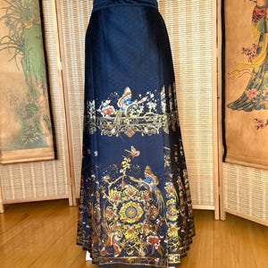 May include: A long, navy blue skirt with an ornate, gold and multi-colored floral and bird design. The skirt features a high waist and a flowing silhouette. The detailed pattern includes butterflies and a repeating circular motif.