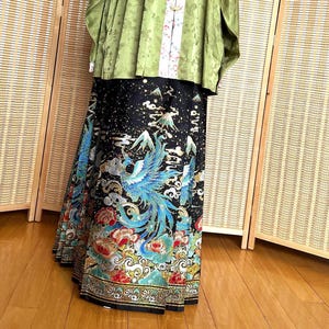 May include: A black skirt with a colorful phoenix design and gold accents. The skirt is made of a silky fabric and has a flowing silhouette.