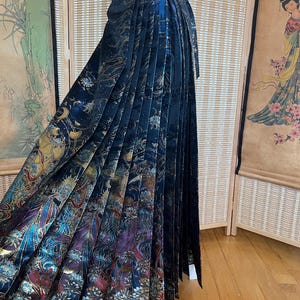 May include: A floor-length, pleated skirt in a deep navy blue fabric featuring a metallic, multi-colored print of celestial motifs, including moons, stars, and swirling patterns. The skirt has a high-waisted design with a wide, structured waistband.