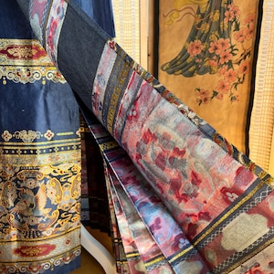 May include: A navy blue garment with ornate gold and red floral patterns. The fabric is folded, displaying a detailed print with red, pink, and grey floral designs. The garment's edge features a gold border. The garment is likely a skirt or dress.