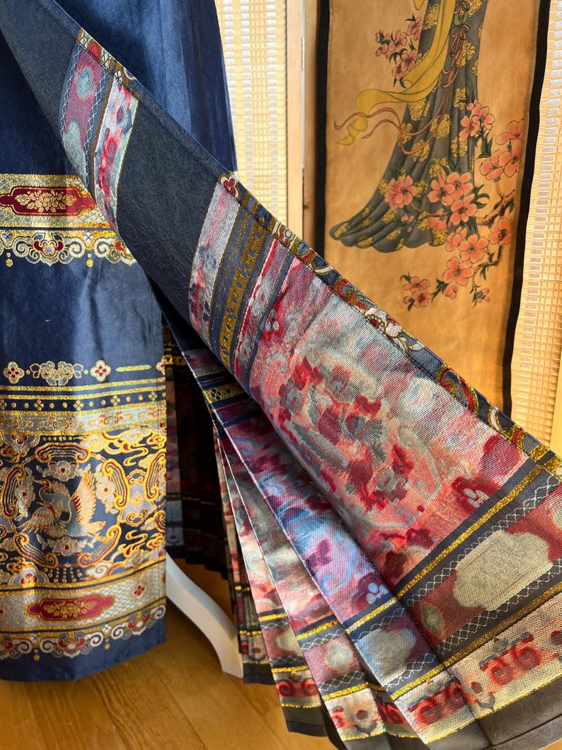 May include: A navy blue garment with ornate gold and red floral patterns. The fabric is folded, displaying a detailed print with red, pink, and grey floral designs. The garment's edge features a gold border. The garment is likely a skirt or dress.
