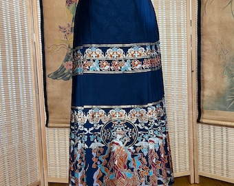 May include: A navy blue skirt with intricate gold, red, and teal patterns. The skirt features a detailed design with floral and figure motifs. The skirt is displayed on a white mannequin, showcasing its full length and design.