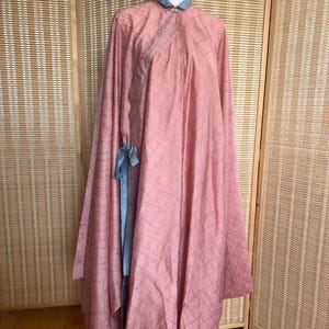 May include: A long, pink robe with a geometric pattern and a blue sash tied at the waist. The robe has a high collar and a button closure at the neck.