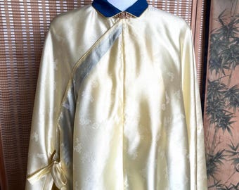 May include: A pale yellow silk robe with a dark blue collar and decorative gold clasp. The robe features a floral pattern and ties at the sleeves. The garment is displayed on a mannequin.
