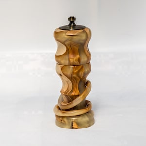 May include: A pepper mill crafted from polished wood with swirling light and dark brown grain patterns. The cylindrical body features a curved, organic shape with a spiraling accent wrapping around the base and a dark metallic knob on top.