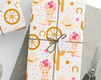 May include: Three gift boxes wrapped in white paper with a pink, yellow, and brown cactus, boot, and wagon wheel pattern. The boxes are tied with twine and have white gift tags attached.