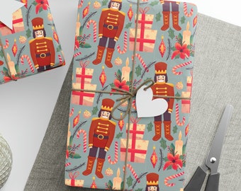 May include: Three gift boxes wrapped in blue and white patterned paper with a nutcracker theme. The paper features red and white candy canes, red and white presents, and red poinsettias. The boxes are tied with twine and have white gift tags attached.