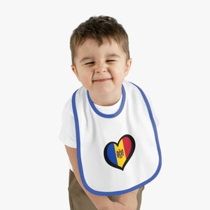 May include: A white baby bib with a blue trim and a heart-shaped design featuring the flag of Moldova. The bib is being worn by a young child with brown hair.