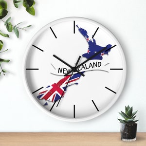May include: White wall clock with black hands and a map of New Zealand with the New Zealand flag on it. The text "NEW ZEALAND" is written on a white banner.