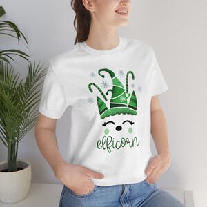 May include: White t-shirt with a green elf unicorn design and the text "elficorn" printed on the front.