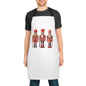 May include: White apron with three red and gold nutcracker soldiers printed on the front.