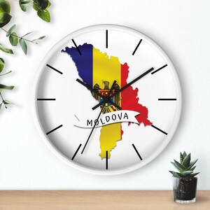 May include: White wall clock with black hands and a white border. The clock face features an outline of Moldova with the Moldovan flag colours and coat of arms. The text "MOLDOVA" is written on a white ribbon.