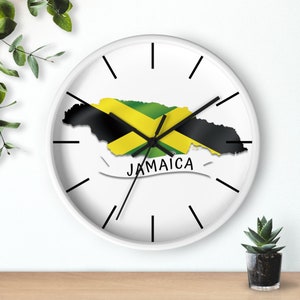 May include: White wall clock with black hands and a black and green outline of Jamaica with the Jamaican flag colours inside. The clock has the word "Jamaica" written in black below the outline.