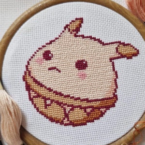 May include: A cross-stitch embroidery hoop with a cute cartoon animal design. The animal is light pink with brown accents and is surrounded by a brown and white patterned border. The hoop is made of wood and has a natural finish.