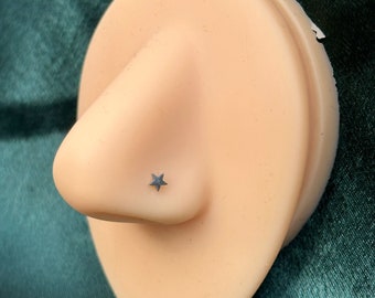 May include: A close-up of a nose piercing on a mannequin. The piercing is a small silver star.