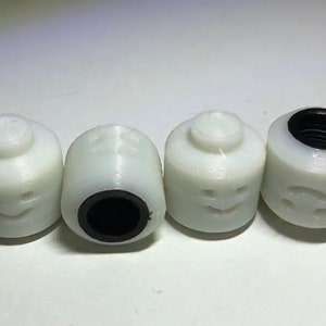 May include: Four white plastic toy heads with different facial expressions. Each head has a black plastic ring around the bottom.