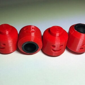 May include: Four red plastic valve stem caps shaped like Lego minifigures with different facial expressions.