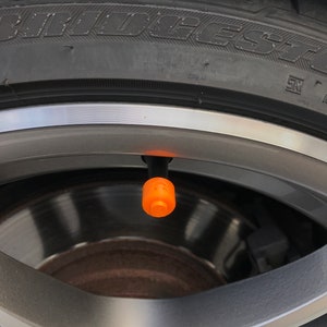 May include: Close-up of a car tyre with a black tyre valve stem cap. The tyre is black with white lettering that reads "BRIDGESTONE".