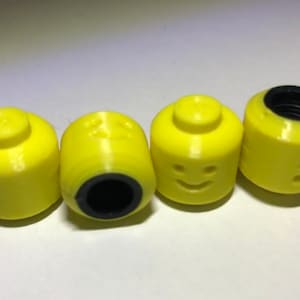May include: Four yellow plastic toy heads with black facial features. The heads are shaped like Lego minifigures and have a hole in the top.