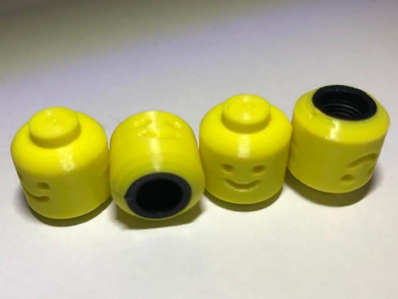 May include: Four yellow plastic toy heads with black facial features. The heads are shaped like Lego minifigures and have a hole in the top.